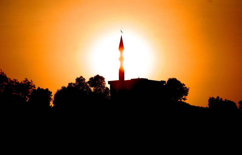 A mosque is silhouetted in front of the sun on a warm autumn day